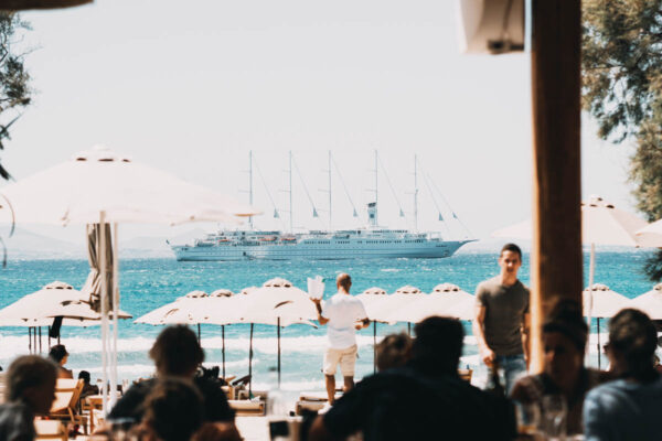 Guests at Naxaki Beach Lounge enjoying a view of a large cruise ship sailing by the beach