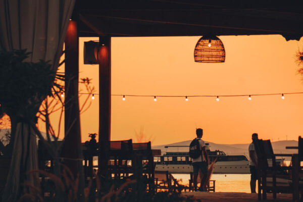 Evening view at Naxaki Beach Lounge with string lights and guests enjoying the sunset by the ocean