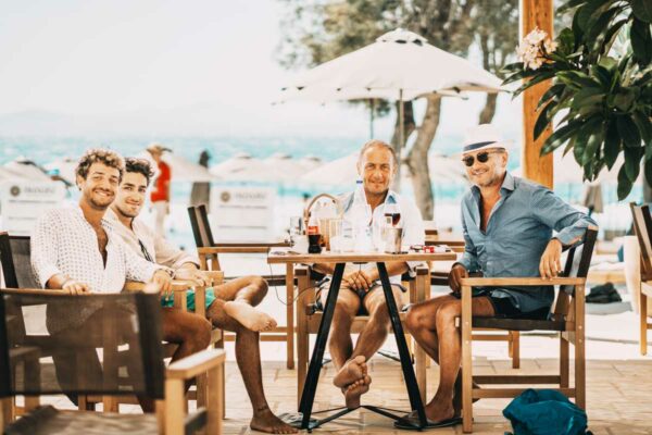 A group of friends dining and relaxing at Naxaki Beach Lounge with the ocean in the background