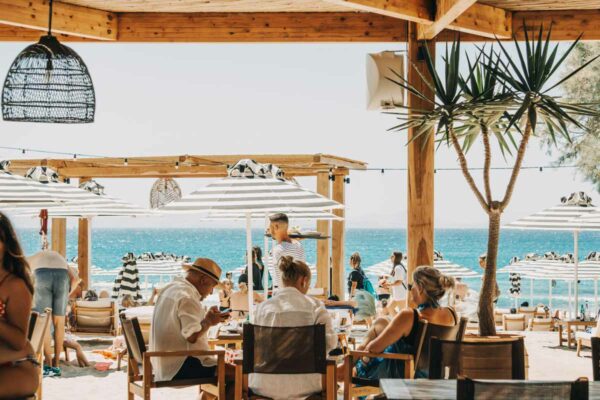 Diners sitting at tables under a bamboo pergola with views of the ocean in the background