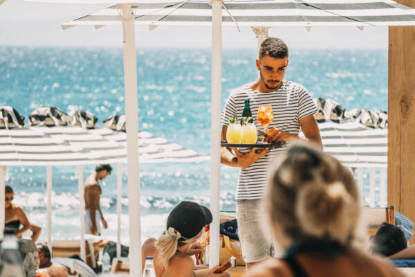 A server offering signature cocktails to customers lounging by the beach