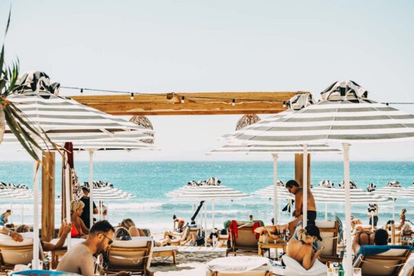 Beachgoers relaxing under striped umbrellas with a clear blue sky and ocean in the background