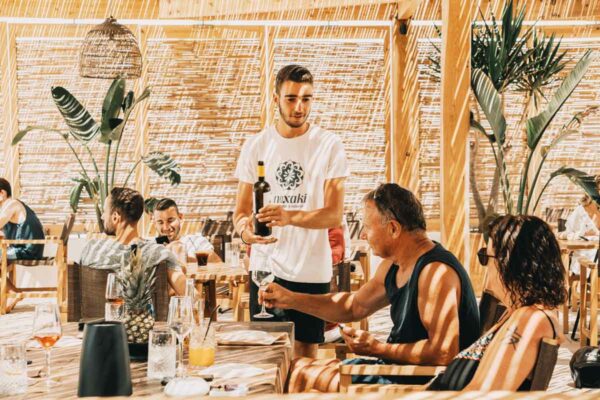 A server pouring wine for guests seated at a table in a naxaki beach lounge restaurant