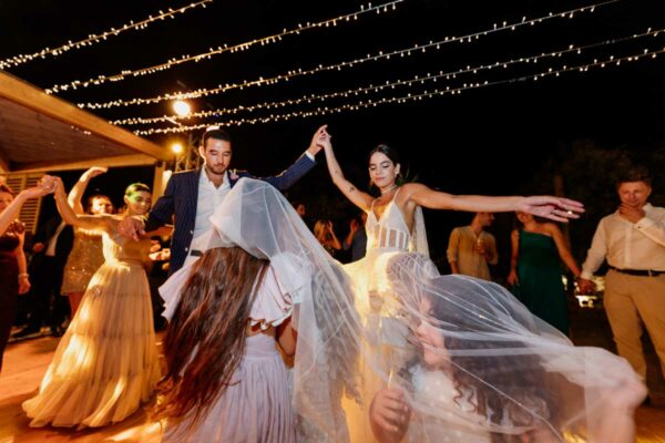 Guests dancing and celebrating at a wedding reception under twinkling lights at Naxaki Beach Lounge and Restaurant