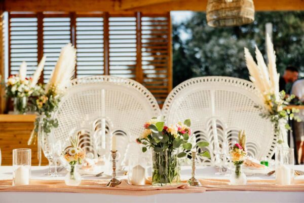 Beautifully decorated head table at a wedding in Naxaki Beach Lounge with floral arrangements and peacock chairs