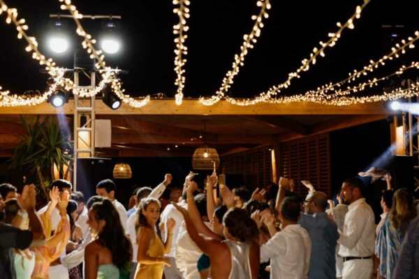 Guests dancing under twinkling string lights during a wedding reception at Naxaki Beach Lounge and Restaurant