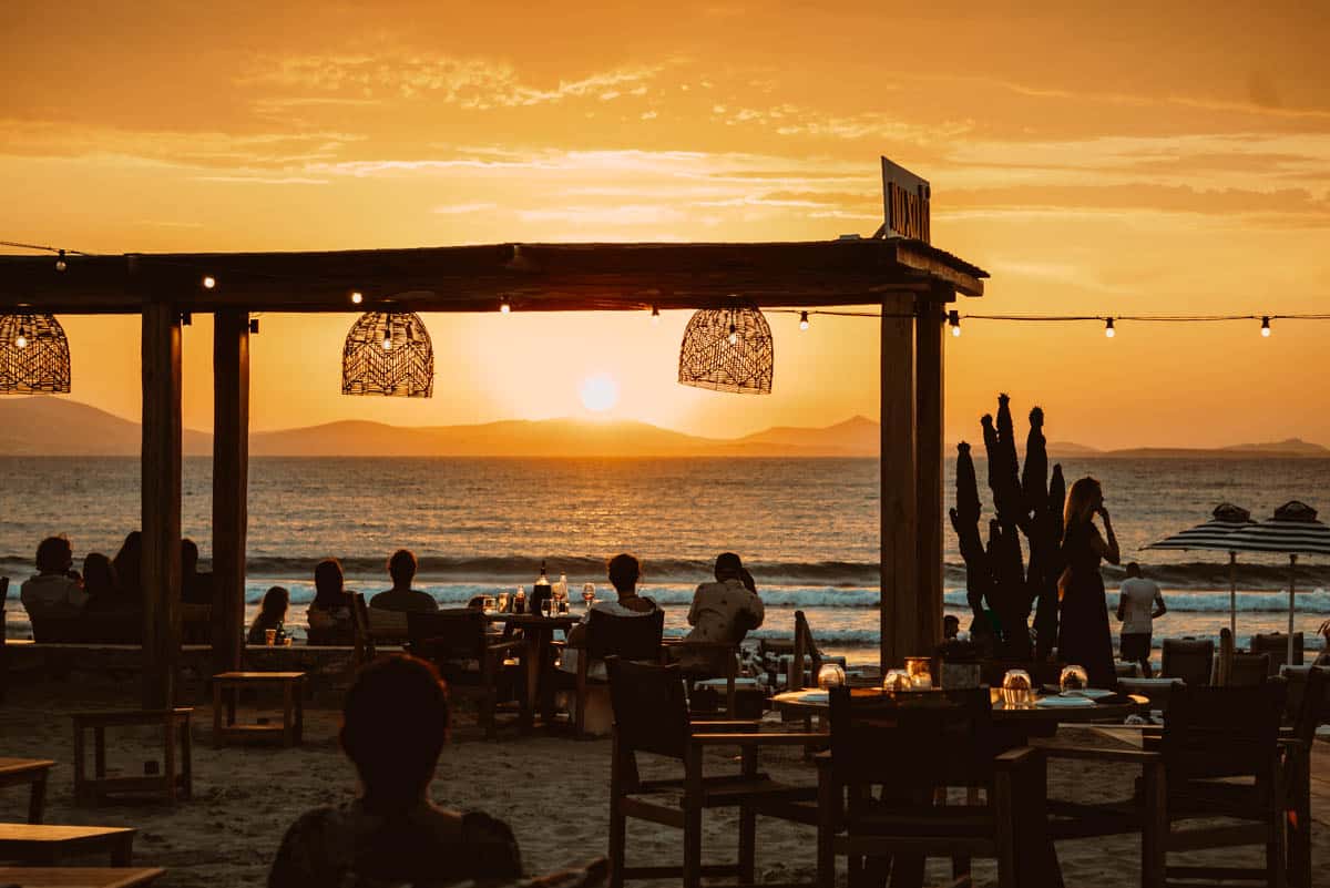Sunset dining at Naxaki Beach Bar & Restaurant on Agios Georgios Beach, Naxos — tables on the sand with views across the Aegean